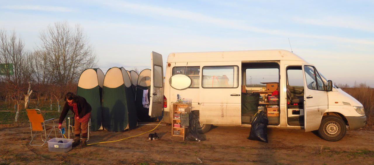 

                          Foto von einem weißen Lieferwagen im Sonnenuntergang, um den herum ein provisorischer Waschbereich mit mobilen Duschen aufgebaut ist.

                          