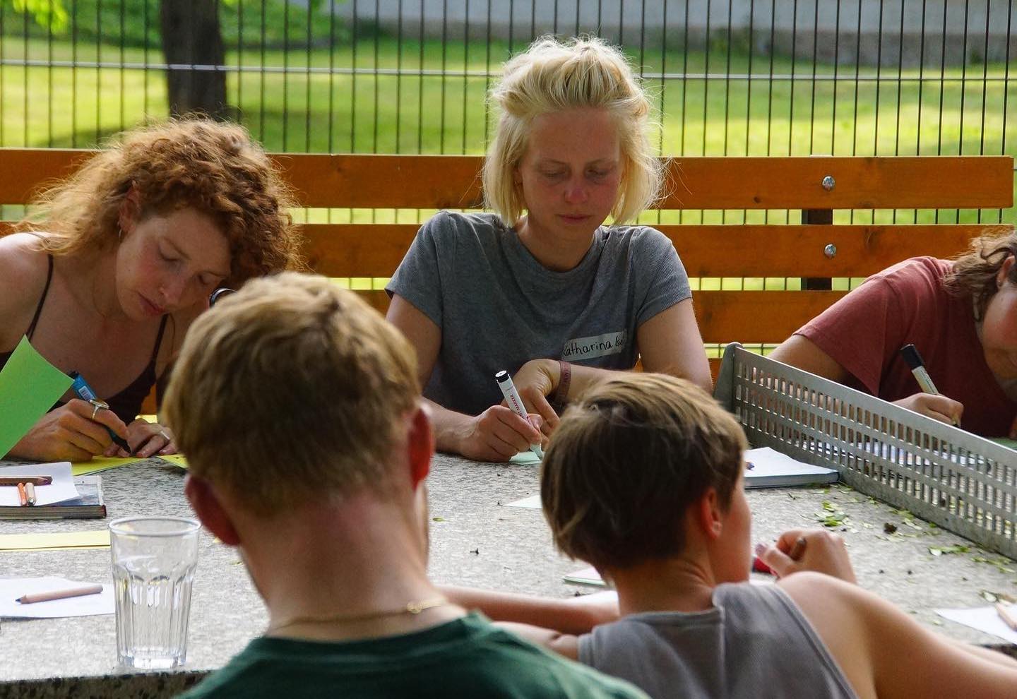 

                          Mehrere junge, weiße Menschen sitzen an einer Tischtennisplatte unter freiem Himmel und machen sich Notizen.

                          
