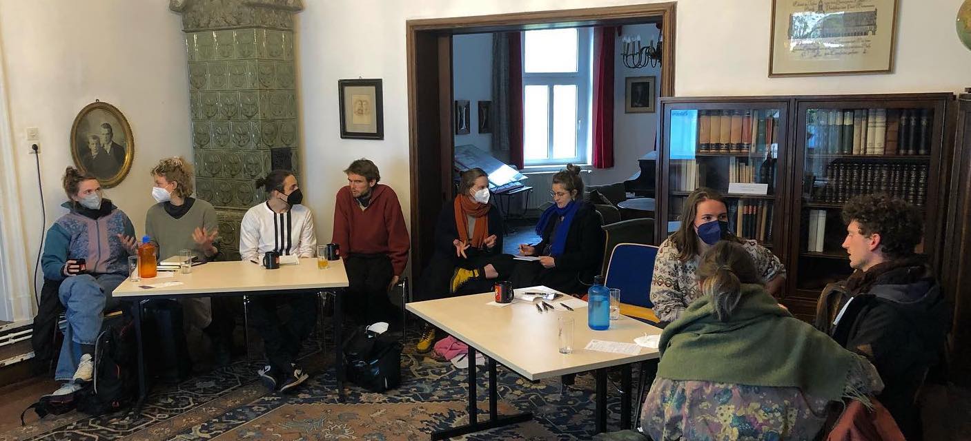

                          Neun weiße, junge Menschen sitzen in einem Raum mit Büchern und einem Kamin und unterhalten sich in Kleingruppen im Rahmen eines Workshops.

                          