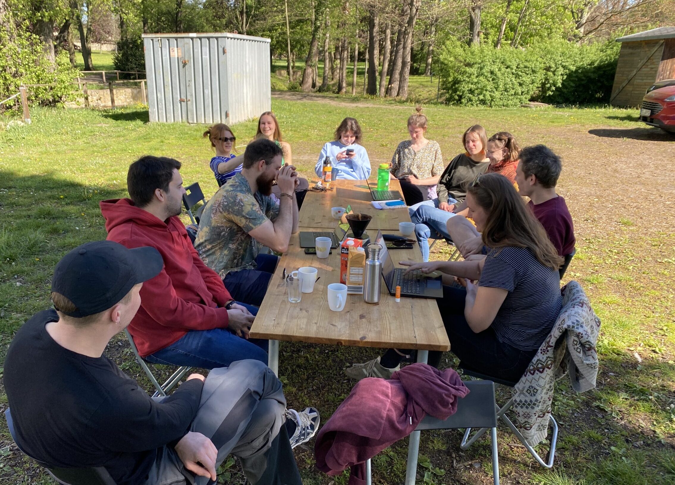 

                          Bild: Einige weiße junge Menschen sitzen um einen Tisch im Freien.

                          