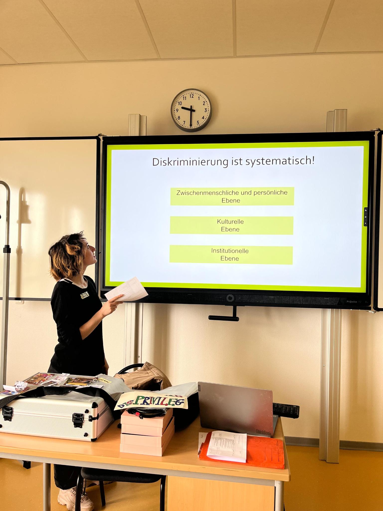 

                          Bild: Eine referierende Person gestikuliert vor einer Power Point Präsentation, welche thematisiert, dass Diskriminierung auf verschiedenen Ebenen systematisch verankert ist.

                          